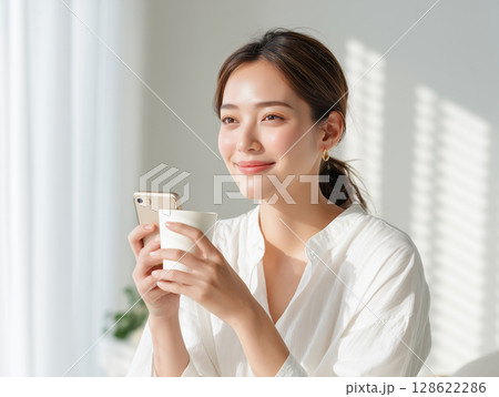 朝の光の中でスマホを見るリラックスした女性 128622286
