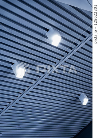 Ceiling with bright lights in a modern warehouse, shopping center building, office or commercial real estate object. Directional LED lights on rails under the ceiling Ceiling with bright lights in a modern warehouse, shopping center building, office or commercial real estate object. Directional LED lights on rails under the ceiling 128622801