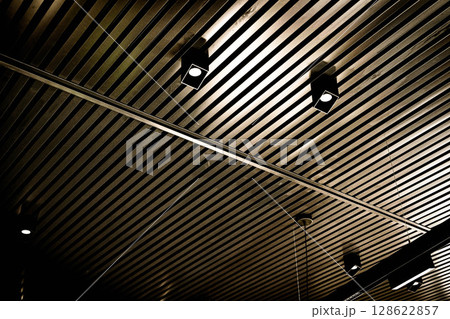 Bottom view of lath ceiling with spot lights. Abstract modern architecture or interior background in black and white with geometric structure. Bottom view of lath ceiling with spot lights. Abstract modern architecture or interior background in black and white with geometric structure. 128622857