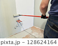 A man paints walls with a roller, working painting on the surface, painting walls in an apartment, repairing with white paint. With space to copy. High quality photo 128624164
