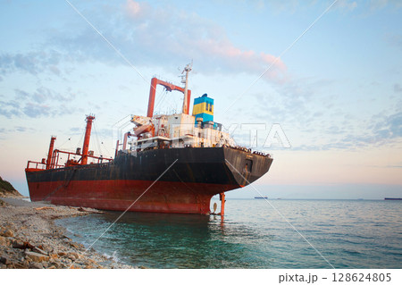 Bulk ship stranded in a sea under sunset sky with white clouds 128624805