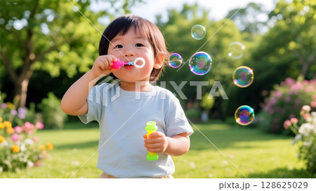 Joyful toddler playing with colorful soap bubbles in sunny green garden on a bright summer day 128625029