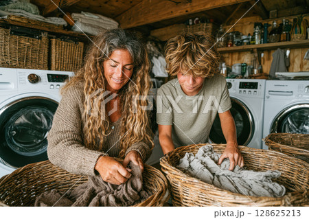Two individuals sorting laundry in a cozy laundry room with baskets and washing machines Two individuals sorting laundry in a cozy laundry room with baskets and washing machines 128625213
