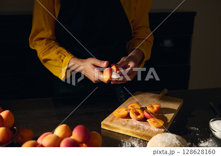 Hands Preparing Fresh Apricots on a Wooden Cutting Board in a Kitchen with Warm Lighting 128628160