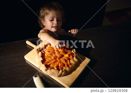 Child Reaching for a Homemade Apricot Galette on Wooden Board Child Reaching for a Homemade Apricot Galette on Wooden Board 128628306