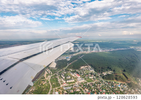 View of airplane wing, blue skies and green land during landing. Airplane window view. 128628593