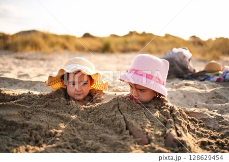 Sisters enjoy a sunny day at the beach while building sandcastles Sisters enjoy a sunny day at the beach while building sandcastles 128629454