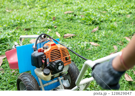 Gardener carefully mowing the green lawn with a modern lawn mower on a sunny day outdoors. Gardener carefully mowing the green lawn with a modern lawn mower on a sunny day outdoors. 128629847