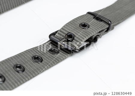 Close up of gray nylon belt with metal buckle, showcasing its durable design and multiple eyelets. belt is laid out on white background, highlighting its texture and functionality Close up of gray nylon belt with metal buckle, showcasing its durable design and multiple eyelets. belt is laid out on white background, highlighting its texture and functionality 128630449