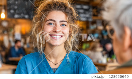 Smiling young woman in blue scrubs sitting at a cafe with warm atmosphere and soft lighting 128630649