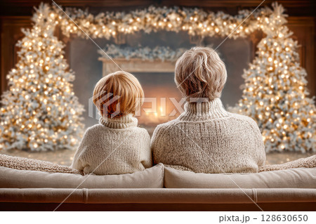 Grandparent and child in cozy sweaters enjoying festive holiday atmosphere by the fireplace 128630650
