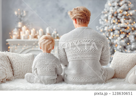 Father and son in matching cozy sweaters enjoying holiday atmosphere by the Christmas tree 128630651