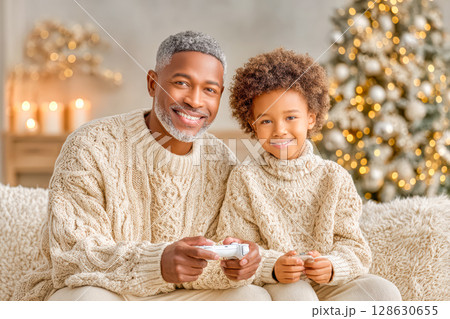 African American man and boy enjoying video game together in cozy holiday setting with lights 128630655