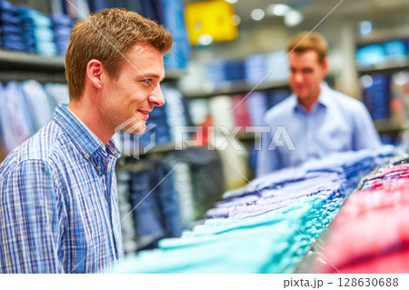 Young man shopping for shirts in clothing store with colorful fabric displays and friendly atmosphere Young man shopping for shirts in clothing store with colorful fabric displays and friendly atmosphere 128630688