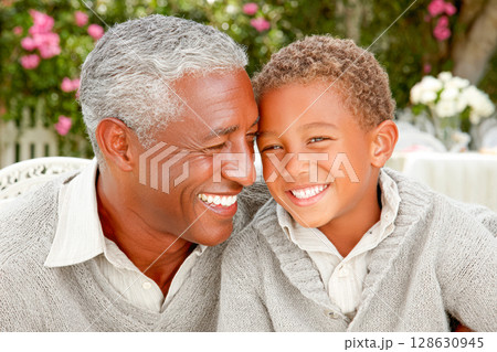Smiling elderly man and young boy sharing joyful moment in cozy outdoor setting with flowers 128630945