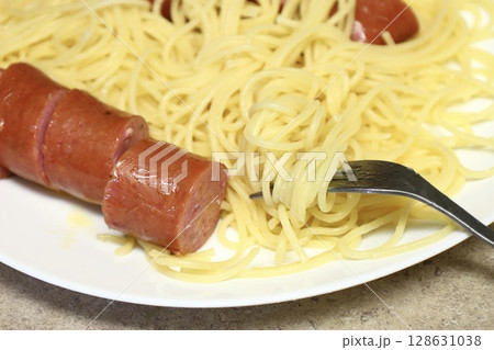 spaghetti with sliced sausage and fork on white plate 128631038