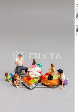 Miniature figurines enjoying a picnic around oversized desserts and fruit pastries 128631654