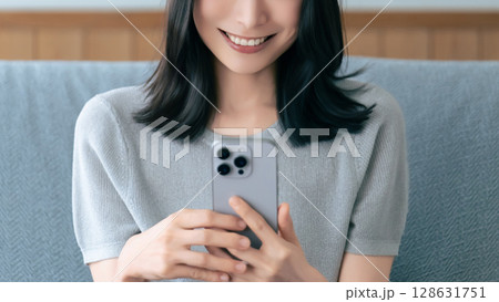 ソファに座ってスマートフォンを使う笑顔の女性 128631751