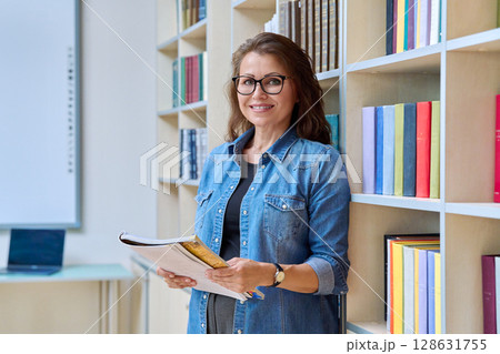 Portrait mature woman teacher, educational behavioral specialist with textbook in classroom Portrait mature woman teacher, educational behavioral specialist with textbook in classroom 128631755