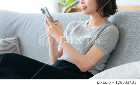 ソファに座ってスマートフォンを使う笑顔の女性 ソファに座ってスマートフォンを使う笑顔の女性 128632433