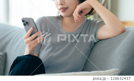ソファに座ってスマートフォンを使う笑顔の女性 ソファに座ってスマートフォンを使う笑顔の女性 128632437