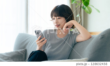 ソファに座ってスマートフォンを使う笑顔の女性 128632438