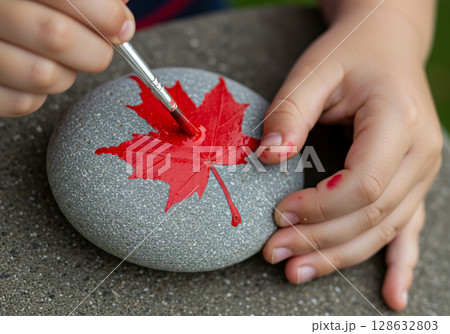 Child painting red maple leaf on stone 128632803