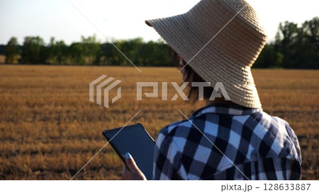Adult farmer using digital tablet at wheat meadow on sunny day. Female agronomist monitoring harvest at barley field. Beautiful scenic landscape. Concept of agricultural business. Slow motion Adult farmer using digital tablet at wheat meadow on sunny day. Female agronomist monitoring harvest at barley field. Beautiful scenic landscape. Concept of agricultural business. Slow motion 128633887