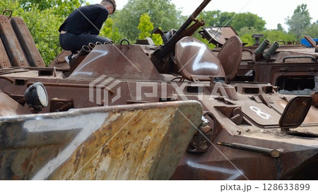Young man looking at destroyed military equipment of the russian army. Exhibition of rusty and burned-out armored vehicles on ukrainian territory. War between Ukraine and russia. Slow motion 128633899