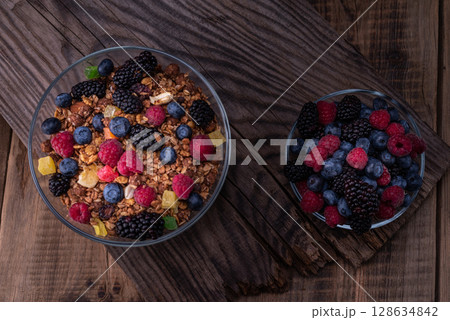 Mix of summer forest berries in a plate. Mix of berries and granola. Glass bowls with berries. Old wooden background. Top. 128634842