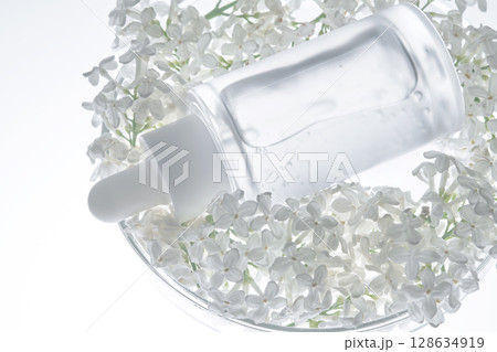 A bottle of serum in a petri dish with white flowers. A bottle of serum in a petri dish with white flowers. 128634919