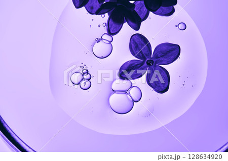 A drop of serum with bubbles and a lilac flower in close-up. A drop of serum with bubbles and a lilac flower in close-up. 128634920