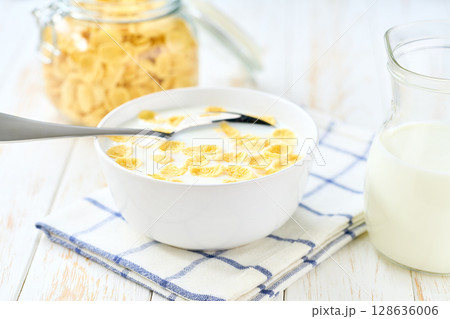 bowl of tasty corn flakes with milk on a light kitchen table. bowl of tasty corn flakes with milk on a light kitchen table. 128636006