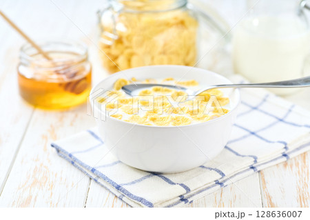 corn flakes in a bowl with milk and honey on a white wooden table. corn flakes in a bowl with milk and honey on a white wooden table. 128636007