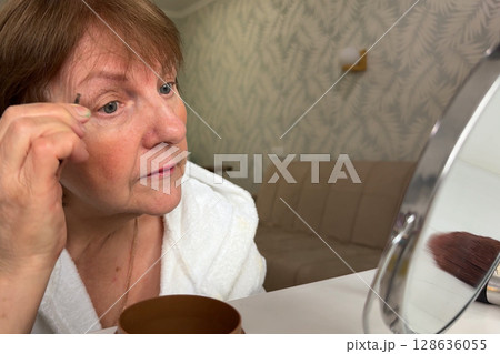 A charming senior woman is at her house, beautifying herself for the morning. A charming senior woman is at her house, beautifying herself for the morning. 128636055