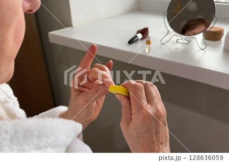 An elderly woman saws her nails at home. The concept of self-care. 128636059