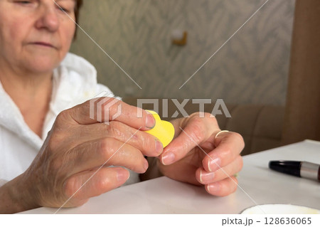 An elderly woman saws her nails at home. The concept of self-care. An elderly woman saws her nails at home. The concept of self-care. 128636065