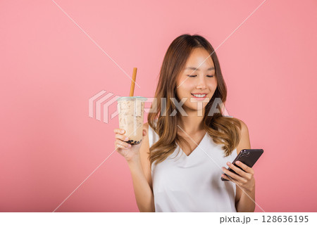 Asian beautiful young woman holding drinking brown sugar flavored tapioca pearl bubble milk tea, Smiling portrait female hold smartphone, studio shot isolated on pink background, milk beverage concept 128636195