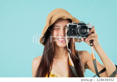 Happy asian woman travel close up, smiling tourist is taking photo with a camera wearing a hat on holiday vacation, she seems happy to travel and take photos, headshots isolated studio blue background 128636432