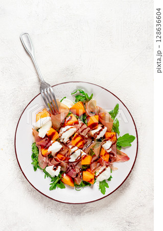 salad with slices of ripe melon, prosciutto, mozzarella and fresh arugula, decorated with balsamic glaze. salad with slices of ripe melon, prosciutto, mozzarella and fresh arugula, decorated with balsamic glaze. 128636604