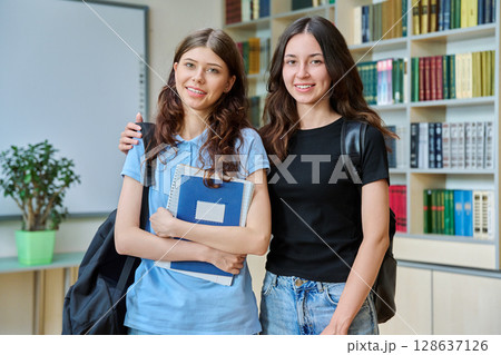 Portrait of two teenage students classmates looking at camera standing in classroom library 128637126