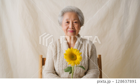 明るい背景でひまわりを抱く高齢女性 明るい背景でひまわりを抱く高齢女性 128637891