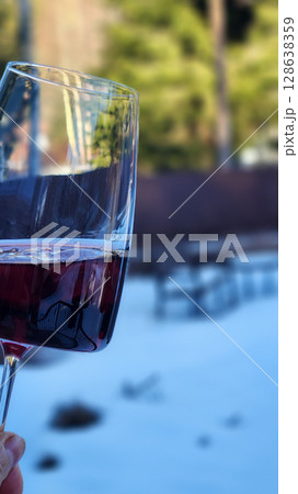 Female hand with glass of red wine against backdrop of nature. Vertical photo. High quality photo 128638359