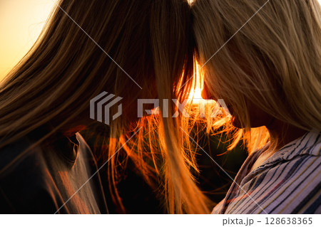Tender sunset moment between mother and teenage daughter touching foreheads, their faces glowing in warm evening light and surrounded by soft strands of hair 128638365