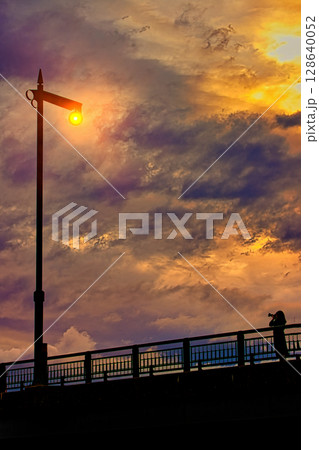 夕焼けの海に立つ街灯を撮影する女性 夕焼けの海に立つ街灯を撮影する女性 128640052