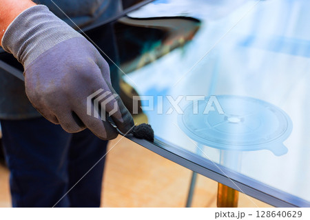Technician carefully coats edge of windshield with adhesive while preparing to replacement windshield 128640629