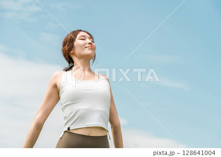 青空の下でストレッチするヨガウェア・スポーツウェアを着た若いアジア人女性 128641004