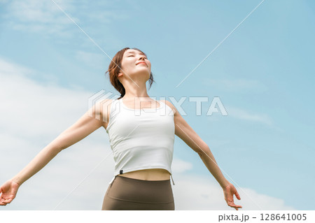 青空の下でストレッチするヨガウェア・スポーツウェアを着た若いアジア人女性 128641005