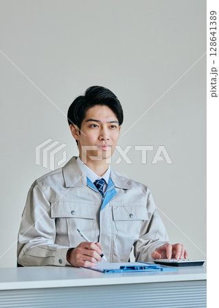 見積書を作成する作業服姿の若い男性 見積書を作成する作業服姿の若い男性 128641389