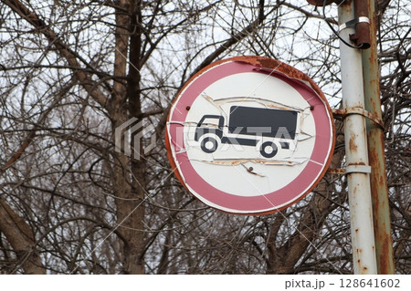 A weathered Truck No Parking sign stands amidst bare trees in a desolate urban landscape 128641602